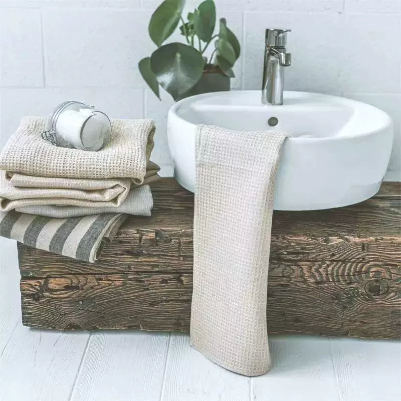 Beige, grey, and white waffle weave cotton towels, set of 4, displayed on a rustic wooden plank next to a white sink.  Rustic bathroom decor.