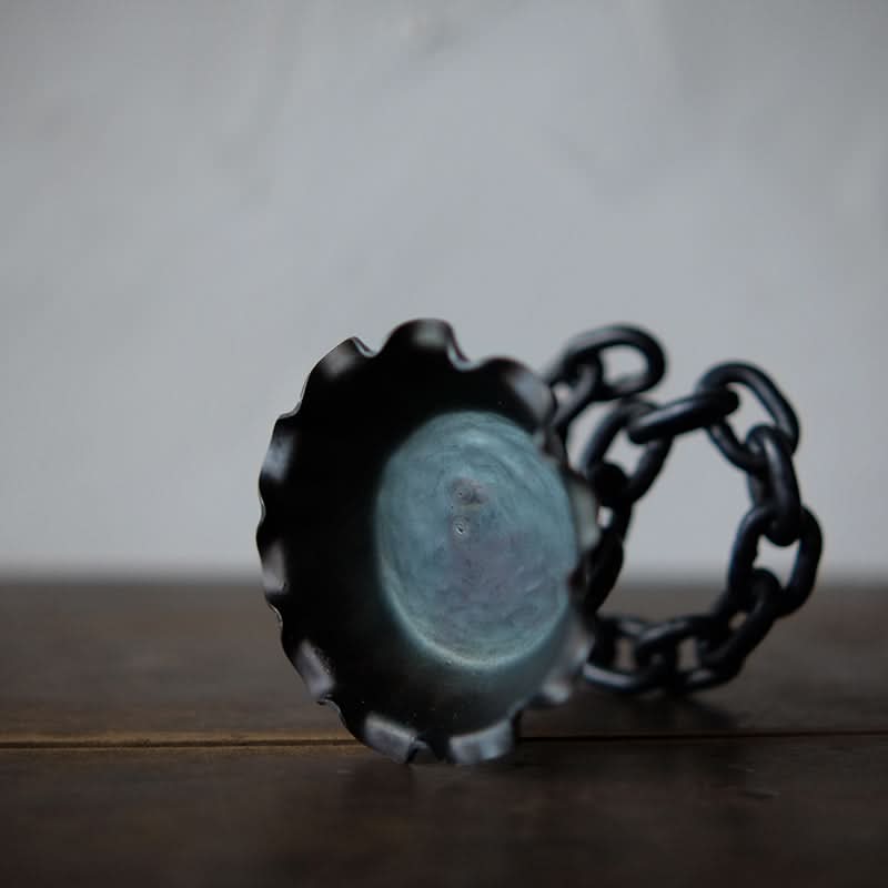 Rustic candle holder with black metal chain design on wooden surface.