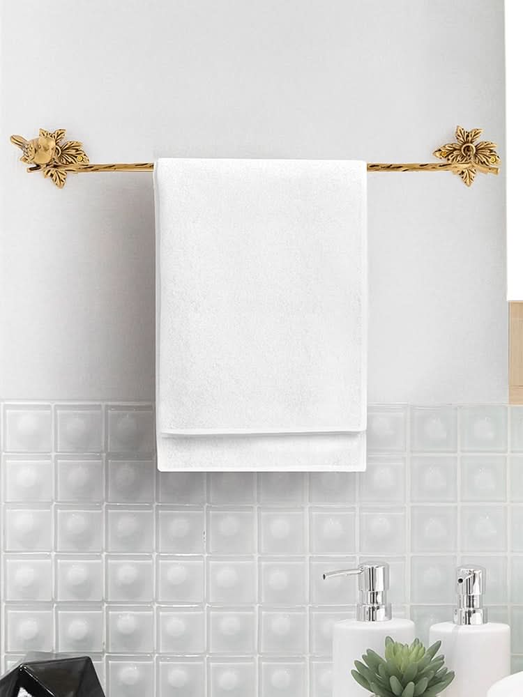 Vintage brass bird branch wall hooks holding a white towel against a textured tile wall.
