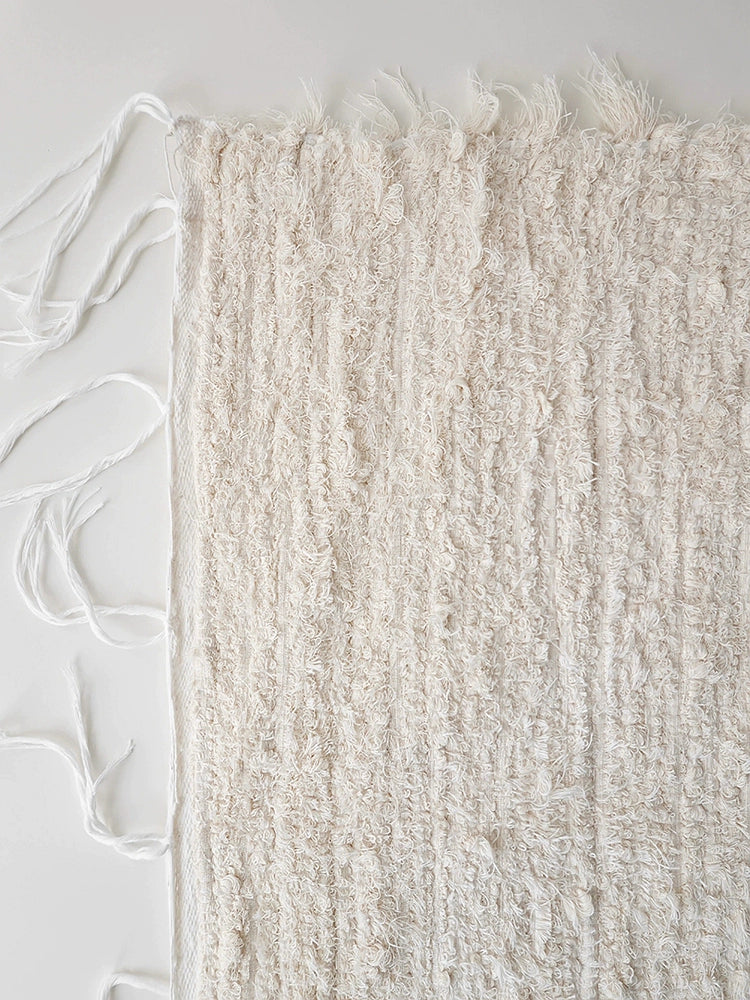Beige knitted throw blanket with textured surface and fringe.  Soft, textured, and cream colored.