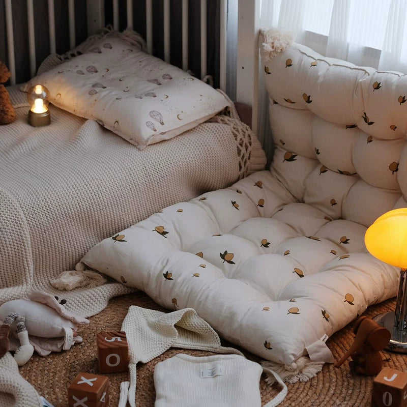 Nursery scene with a tufted floor cushion featuring small brown tree/leaf pattern next to a crib.