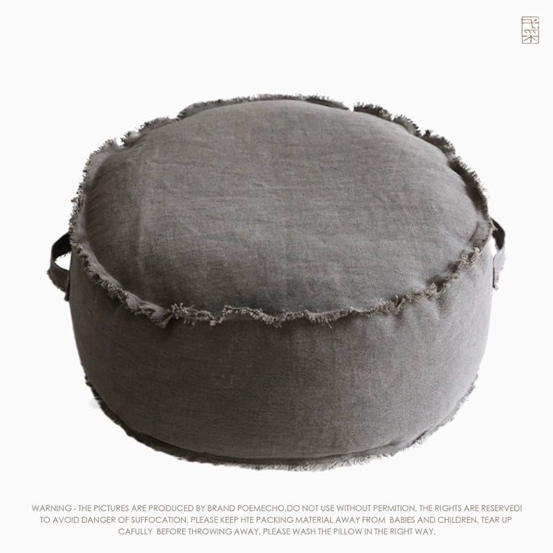 Round gray fabric ottoman pouf with frayed edges, decorative accent seating.