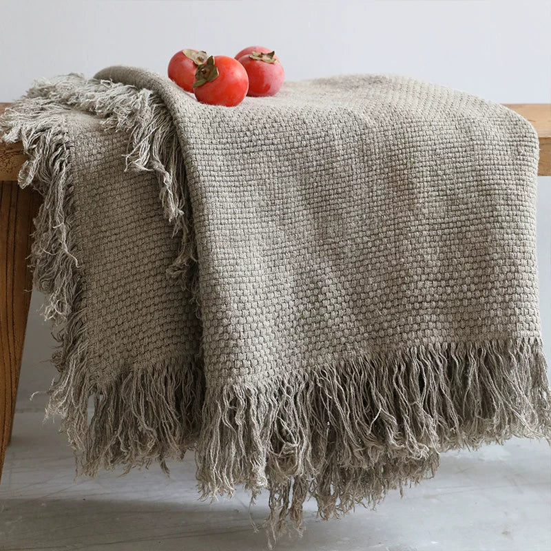 Textured Linen Throw Blanket with Fringes in taupe, draped over a wooden surface with persimmons.