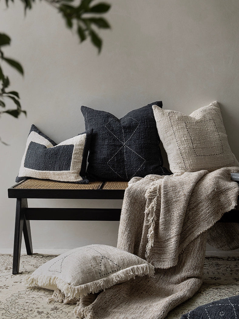 Boho throw pillows & blanket set: beige, black, natural woven cushions with fringed detail on bench.