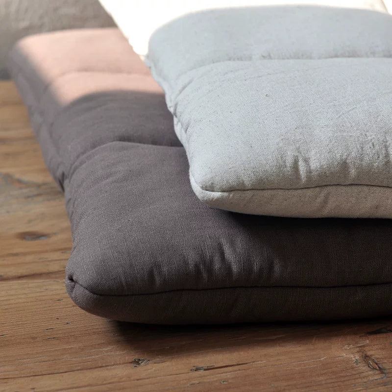 Close-up of stacked floor cushions, one dark brown and one light cream, on a wooden surface.
