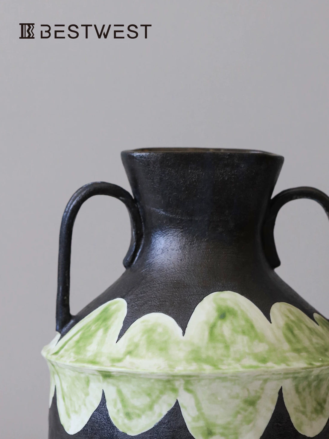 Close-up of a designer ceramic vase showing textured black finish and painted green scalloped detailing