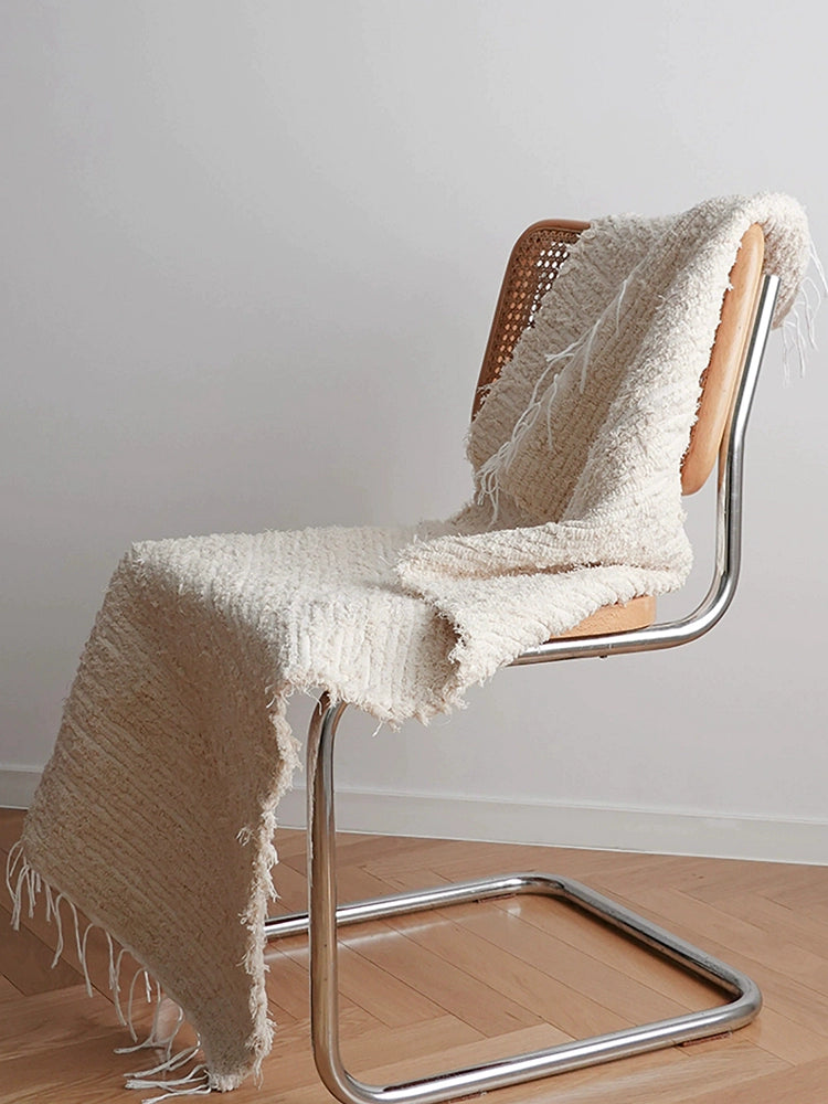 Beige knitted throw blanket with fringe, draped over a light wood chair.  Soft texture, boho style.
