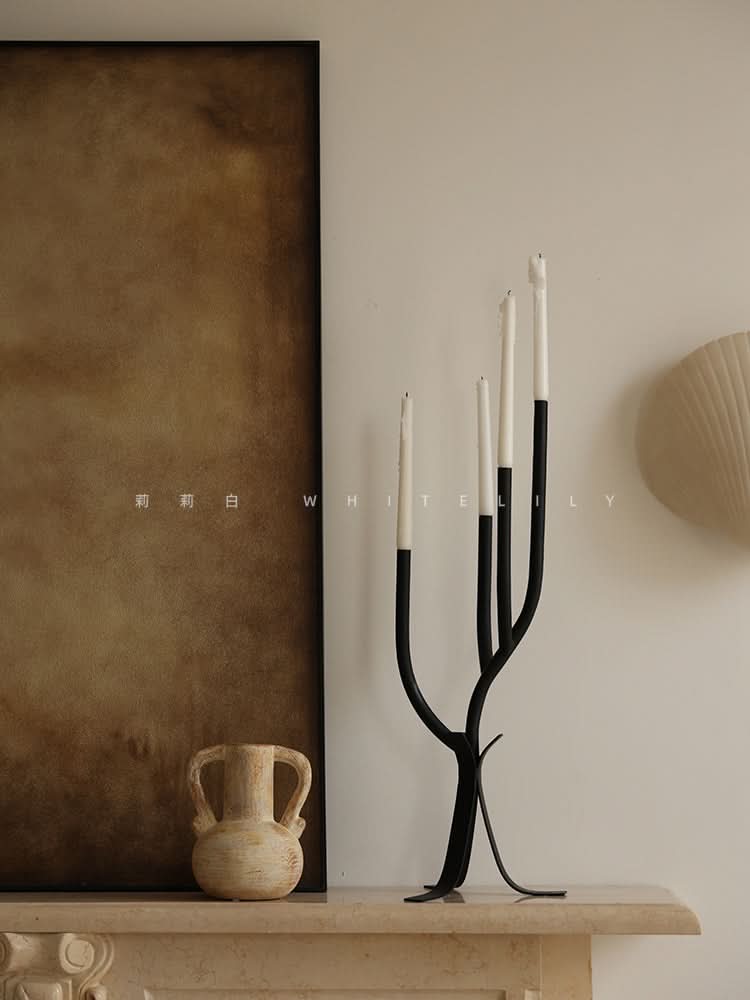 Modern Branch Candle Holder with white candles, black metal base, on marble shelf.