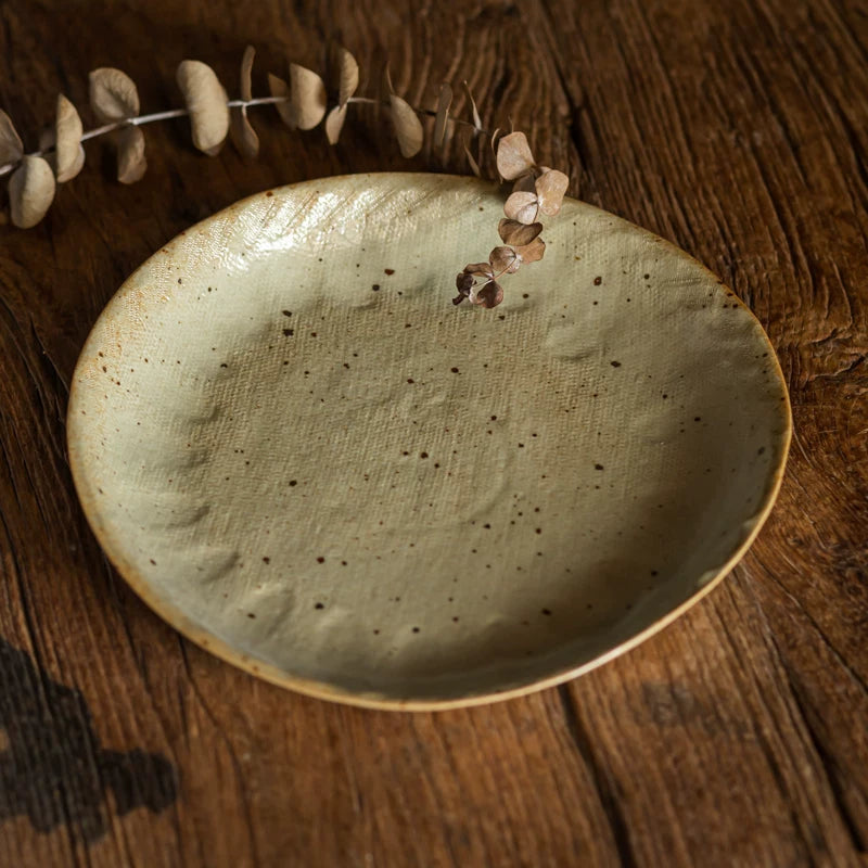 Close-up of a speckled, pale green ceramic plate with a rustic, uneven rim resting on dark wood.