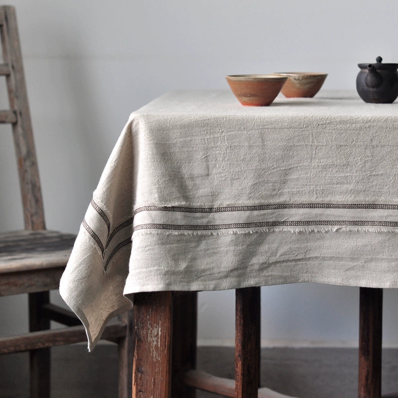 Rustic Linen Tablecloth with Striped Border, natural beige, on wooden table with rustic chair and bowls.