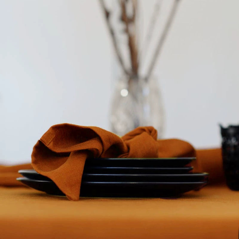 Elegant Linen Table Napkins in burnt orange, knotted, on black plates.