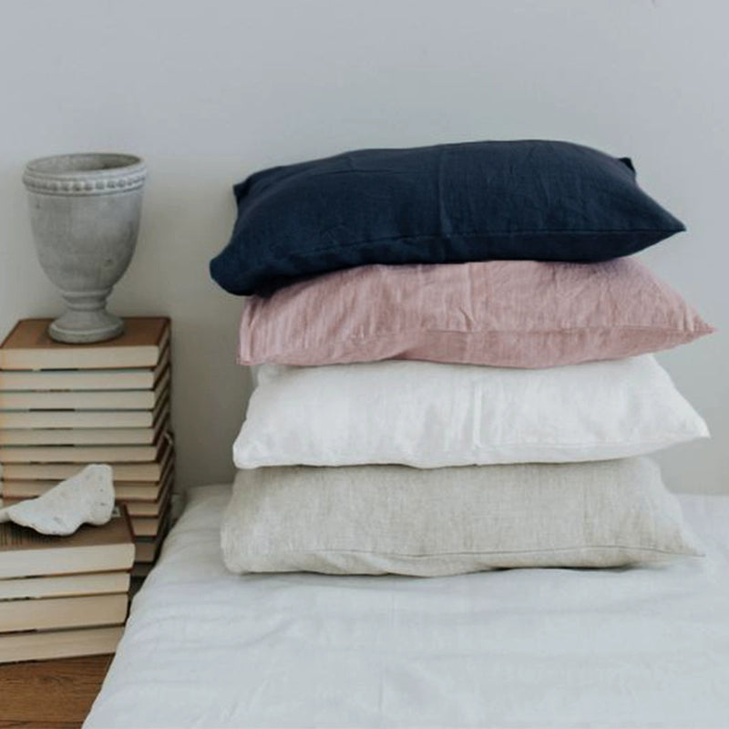 Stack of elegant linen pillow cases in navy, rose, white, and natural.