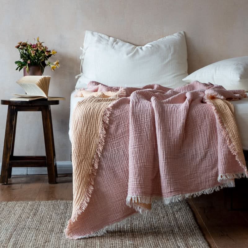 Pink & peach breathable cotton throw blanket draped on a bed. Cozy home decor.