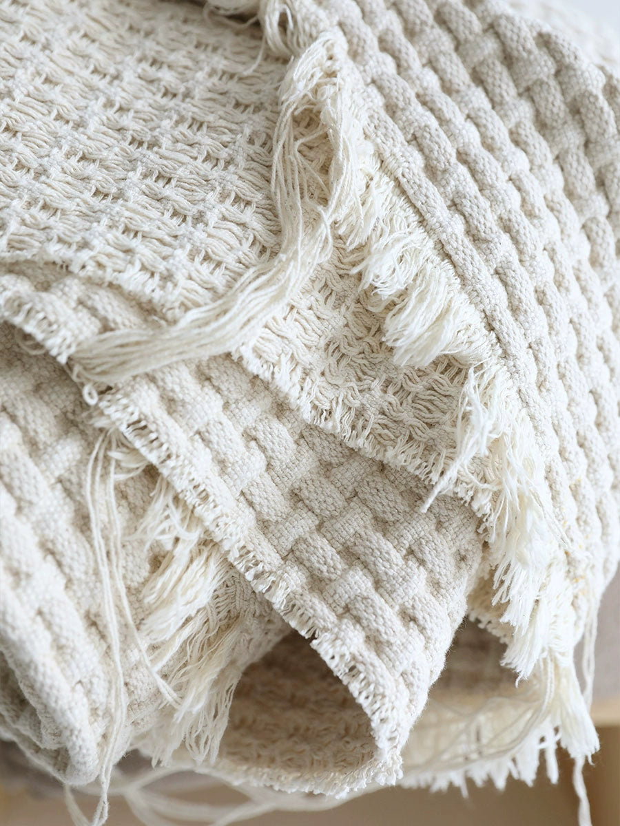Beige woven cotton throw blanket with textured squares and frayed edges.
