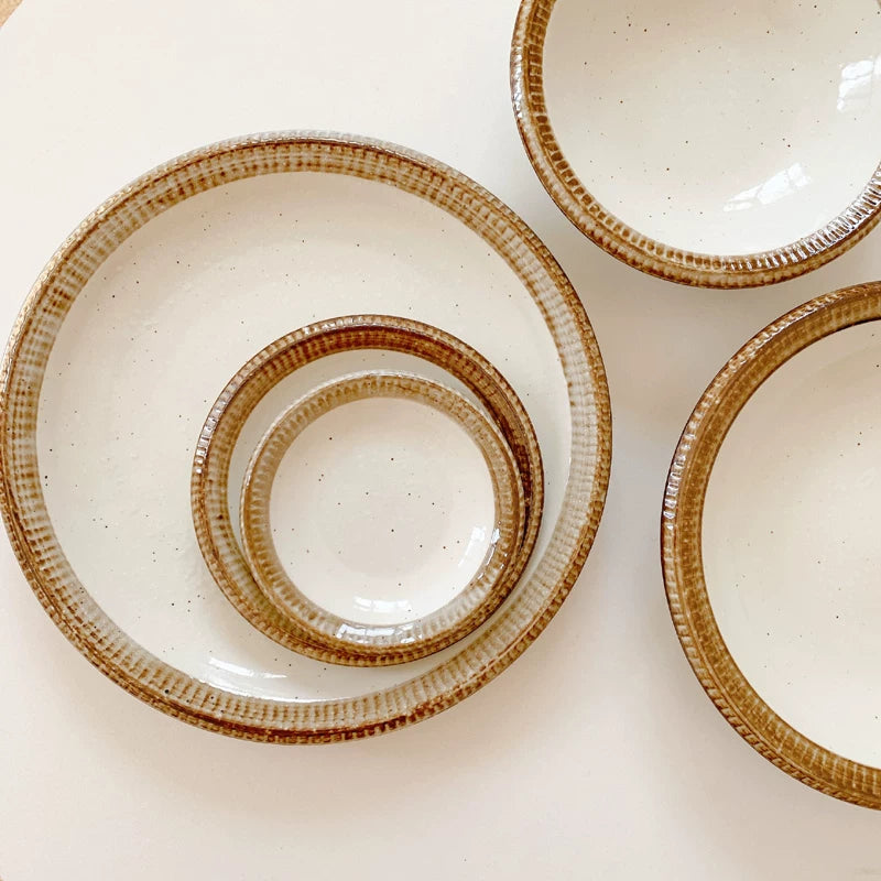Stack of three ceramic plates with speckled white glaze and wide, textured brown rims.