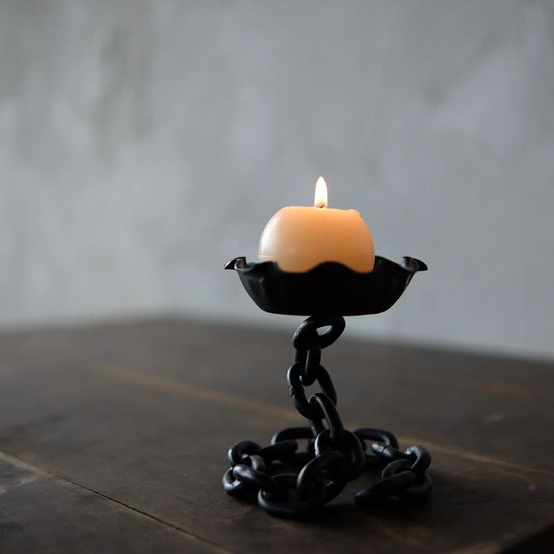 Rustic candle holder with chain design, black metal, lit candle on dark wood table