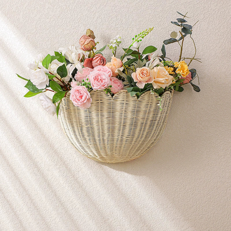 Beige scalloped wicker wall basket, filled with flowers, hanging on a light beige wall.  Woven wicker, decorative.