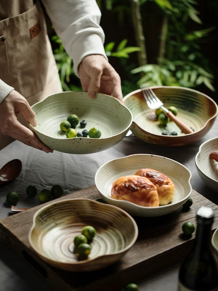 Person holding two speckled ceramic bowls, one sage green and one brown swirl, filled with vegetables.