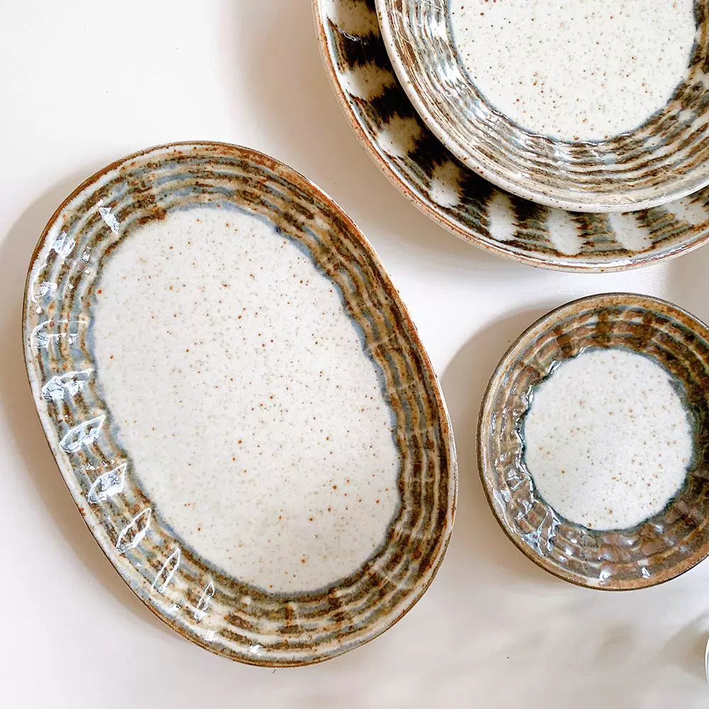 Close-up overhead view of an oval ceramic serving plate with speckled center and wide, textured brown rim.