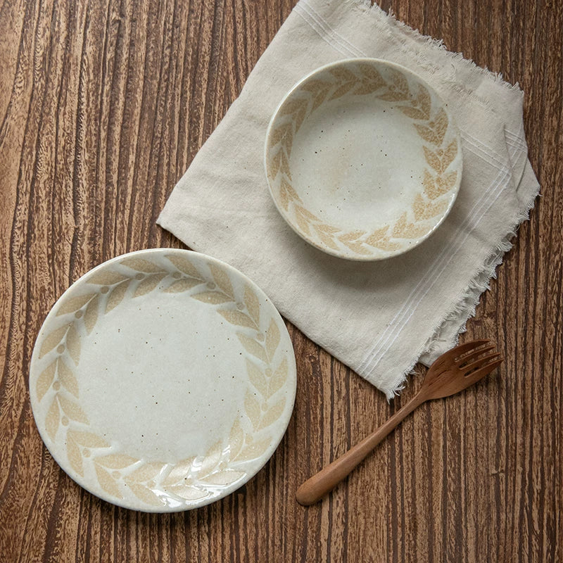 Overhead view of a ceramic plate and matching small bowl on a linen cloth.