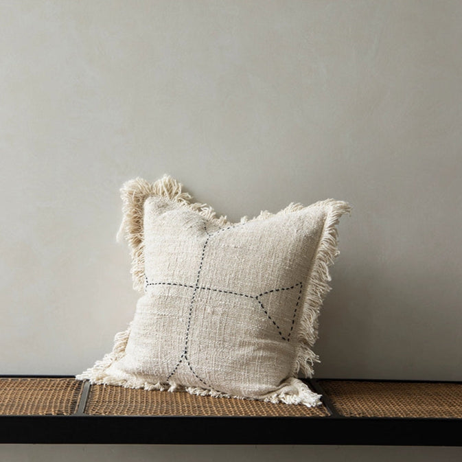 Boho throw pillow: beige woven cushion with black stitching and fringe accents.