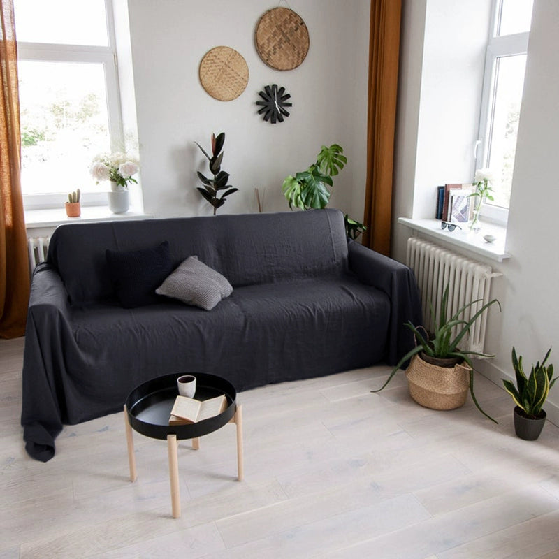 Mustard yellow linen sofa throw blanket draped over a dark grey sofa with pillows. Cozy living room decor.