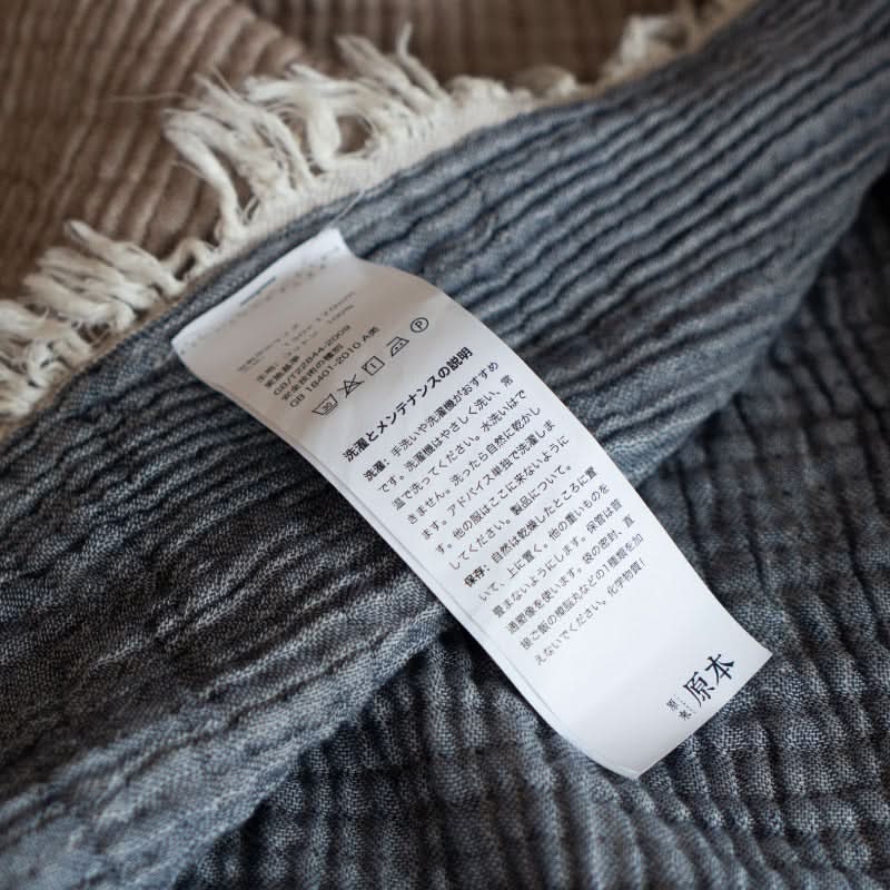 Close-up of a breathable cotton throw blanket in gray and beige, showing the care label.