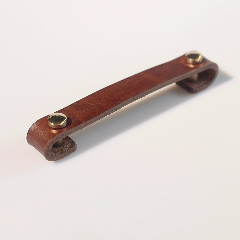 Brown leather drawer pull with brass fasteners on white background. Rustic cabinet handle.