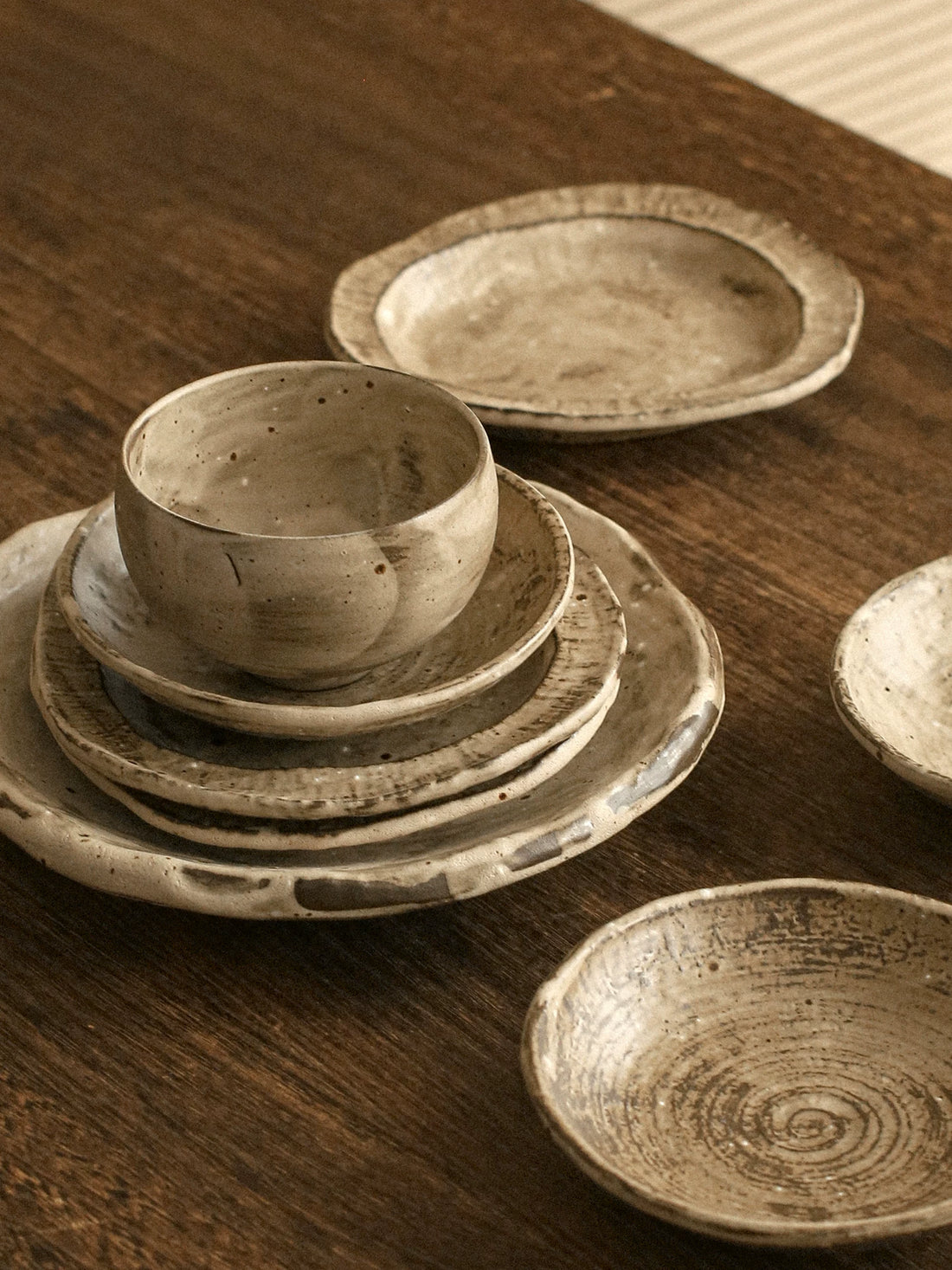 A handmade coarse pottery bowl and matching saucer featuring an irregular rim and mottled texture.