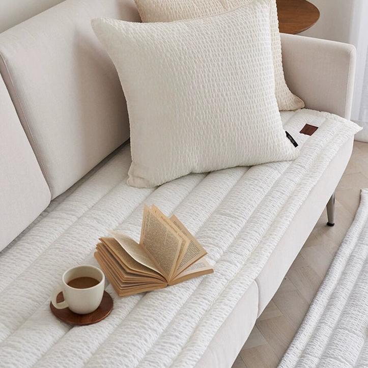 White quilted sofa protector and rug set.  Cozy, textured, and stylish.  Matching rug and protector.  Open book and coffee cup on top.