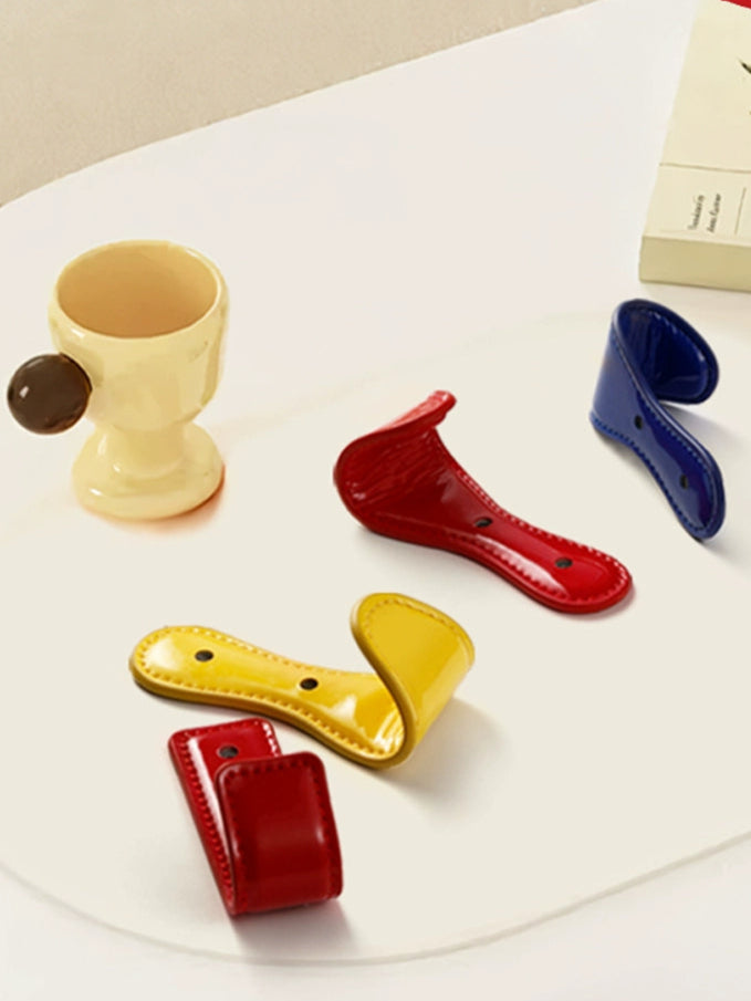 Colorful leather wall hooks in red, yellow, and blue dopamine decor colors with a cream ceramic holder.