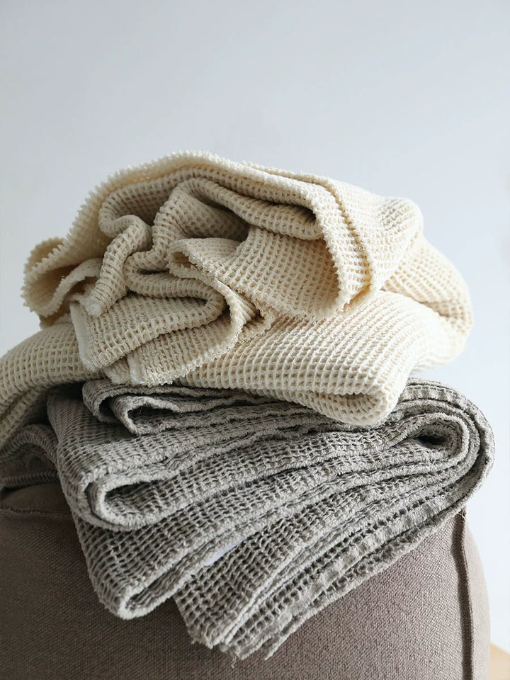 Stacked waffle knit linen throw blankets, beige and gray.