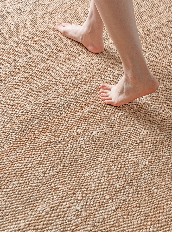 A close-up of a person's feet stepping onto a natural fiber rug with a textured weave and a subtle pattern.