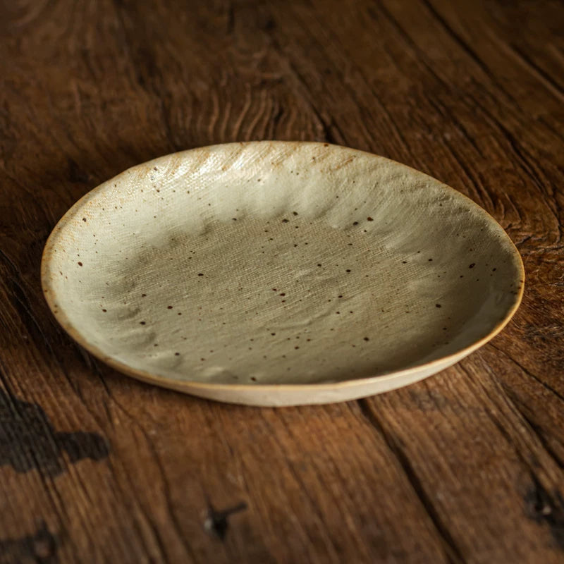 A pale, speckled green ceramic serving plate with hand-pinched rim details on a wooden surface.