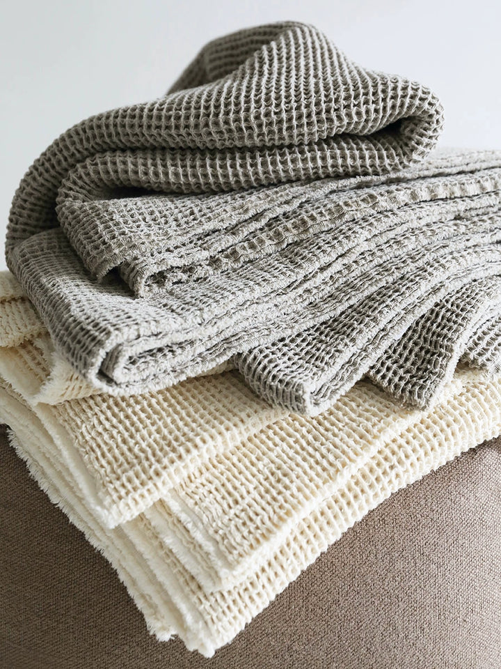 Stacked waffle-knit linen throw blankets, beige and gray.  Soft, textured, and cozy.