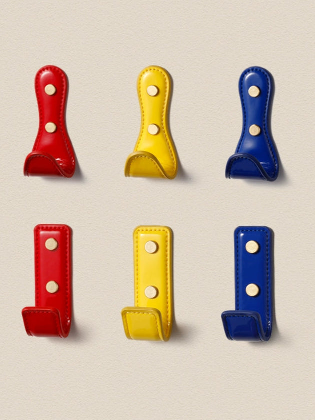 Colorful leather wall hooks in red, yellow, and blue. Dopamine decor colors.