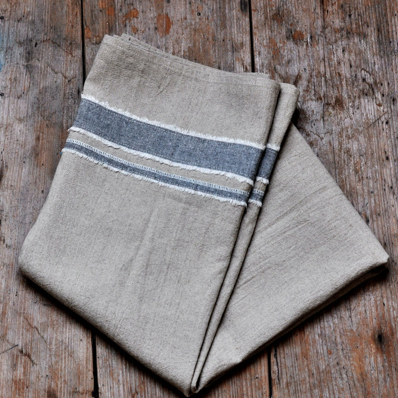 Rustic linen tablecloth with blue striped border and frayed edges, on wooden surface.