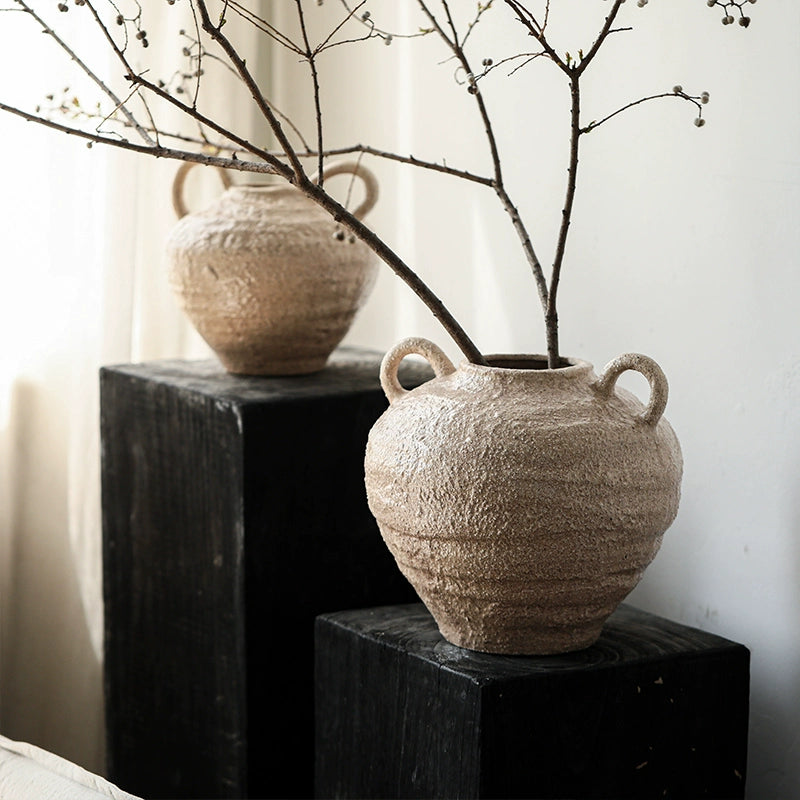 Rustic ceramic vase with handles, handcrafted beige pottery on black wooden pedestals