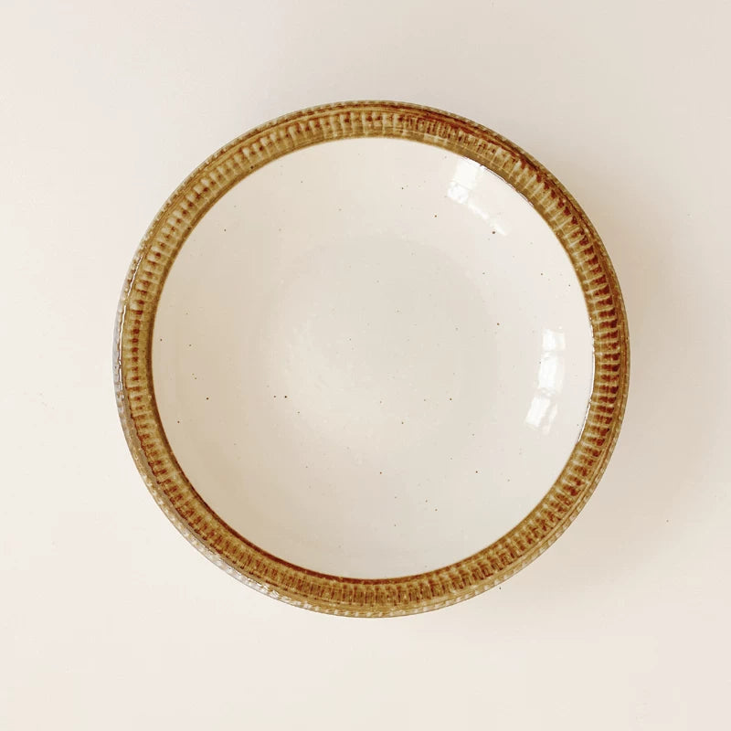 Close-up of a ceramic bowl showing the speckled interior and the wide, ribbed brown edge.