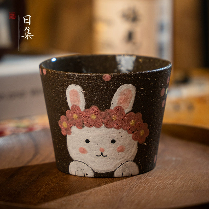 Hand-painted Japanese ceramic tea cup with a cute bunny design and floral wreath, perfect gift.