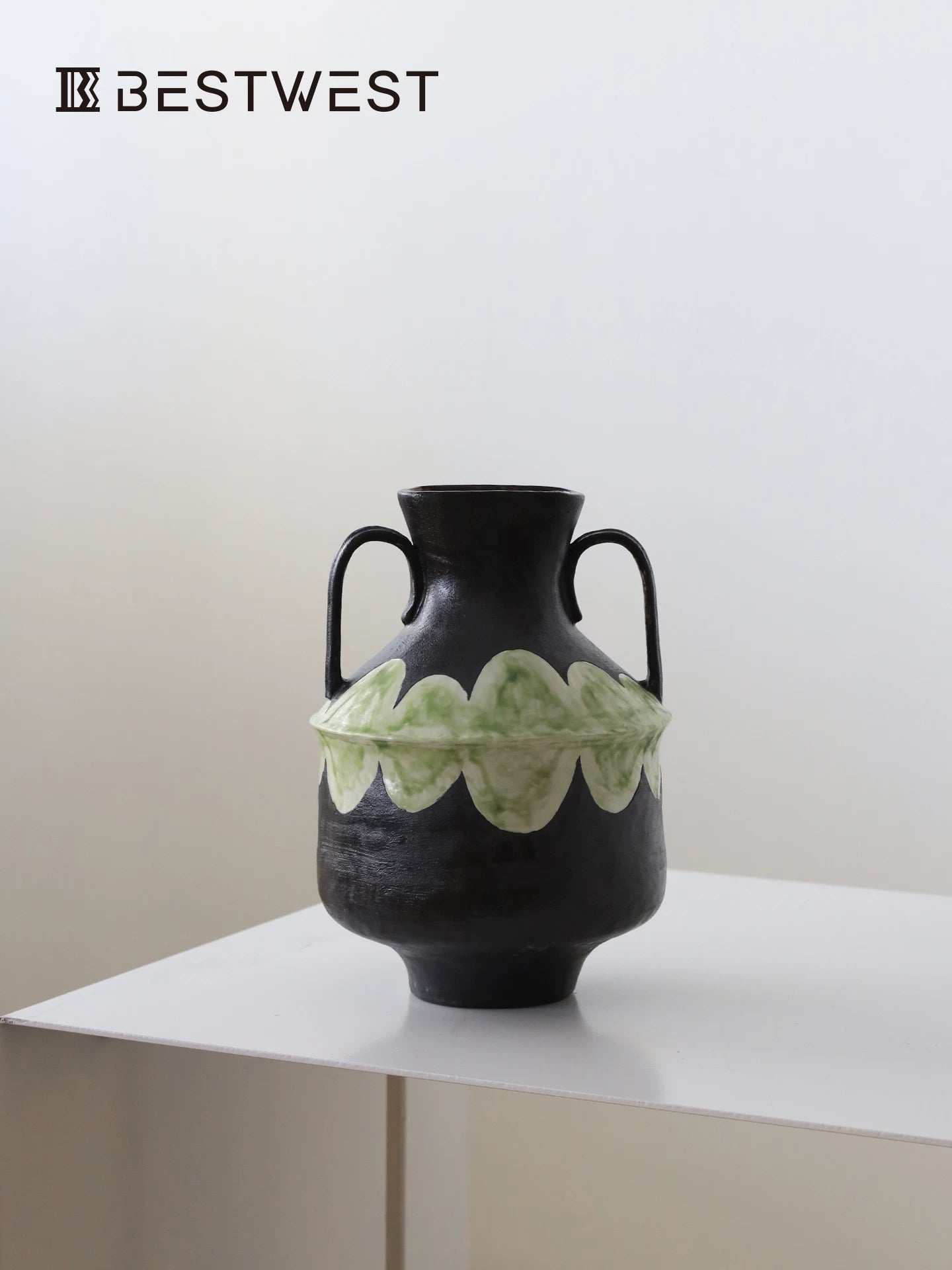 Studio shot of a modern black ceramic vase with green scalloped decorative band on white surface