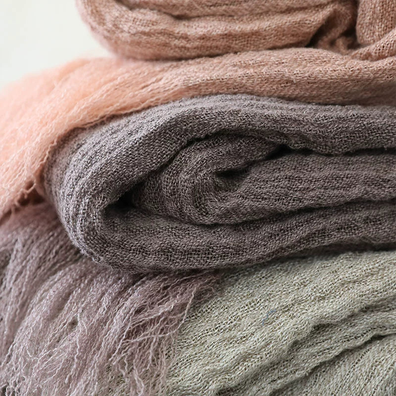 Stacked linen throw blankets in muted tones of taupe, rose, and beige.  Soft, textured fabric with delicate fringes.