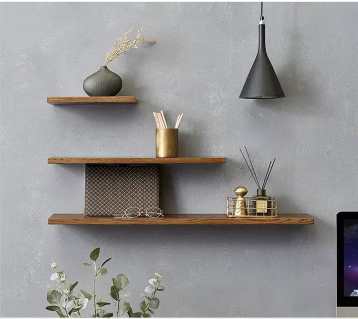 Three tiered dark wood floating shelves mounted on a gray textured wall with decorative items.