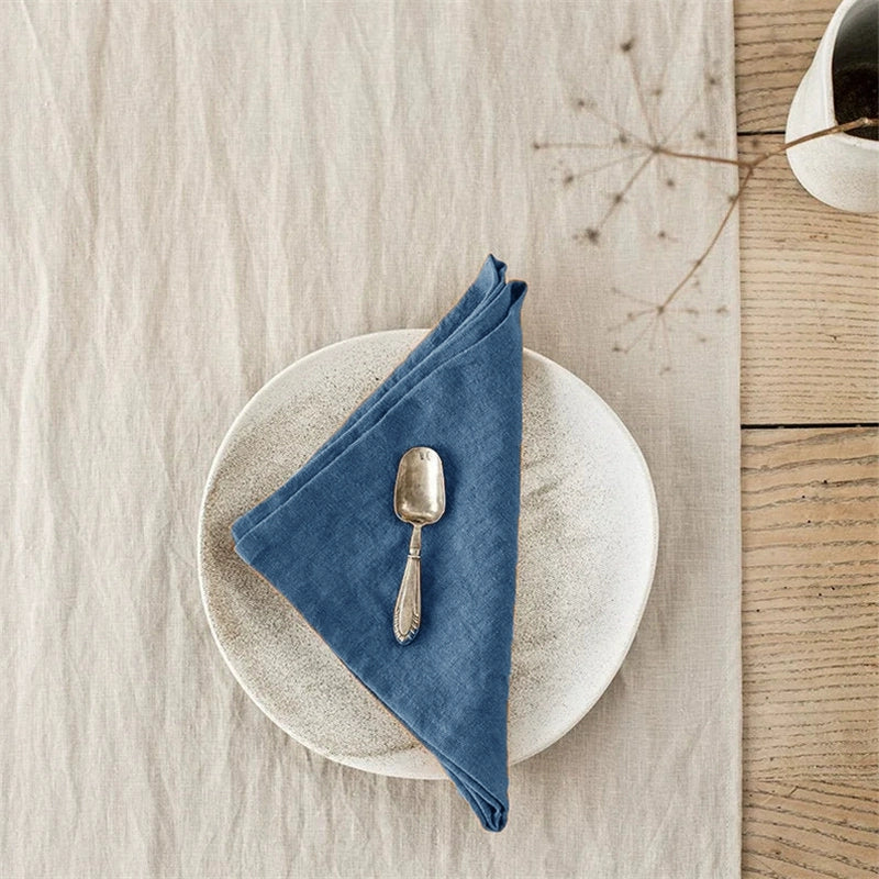 Blue elegant linen table napkins, knotted, on a textured plate with a spoon.
