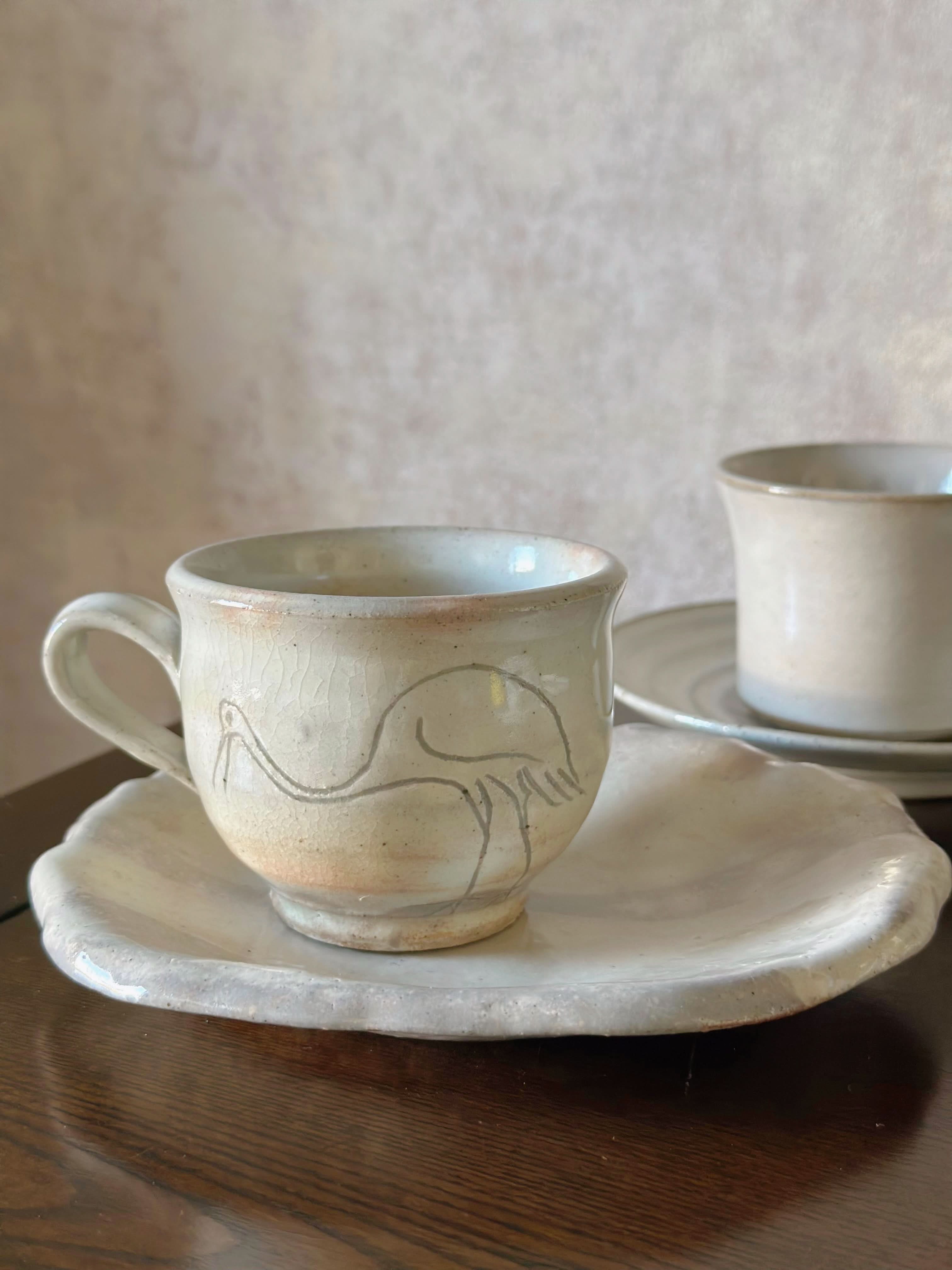Hand-thrown Japanese vintage teacup & saucer, cream ceramic with bird design, on dark wood.