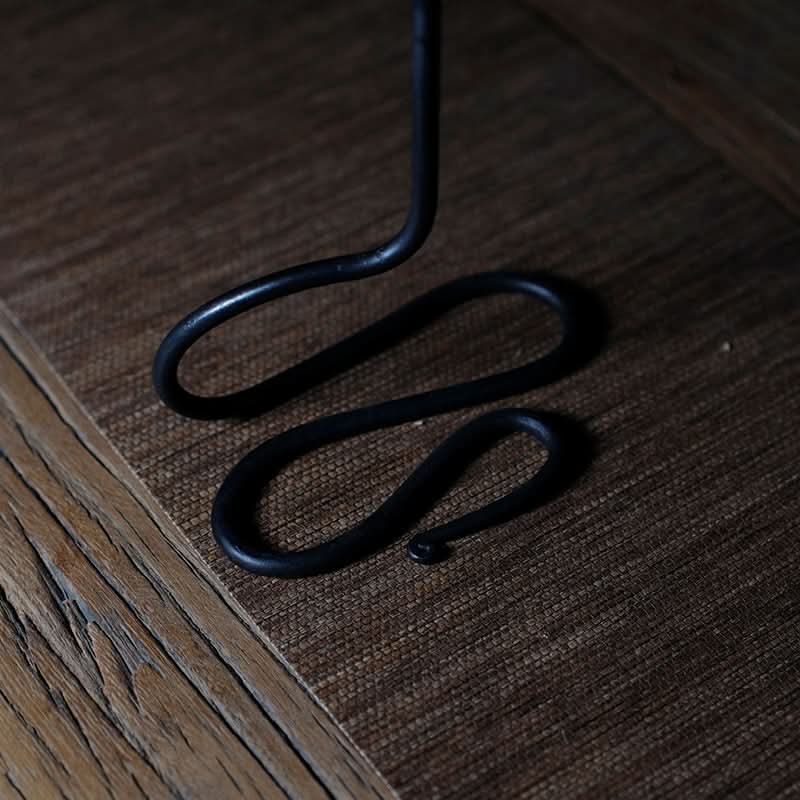 Black Metal Curved Candle Holder on rustic wood and woven surface.