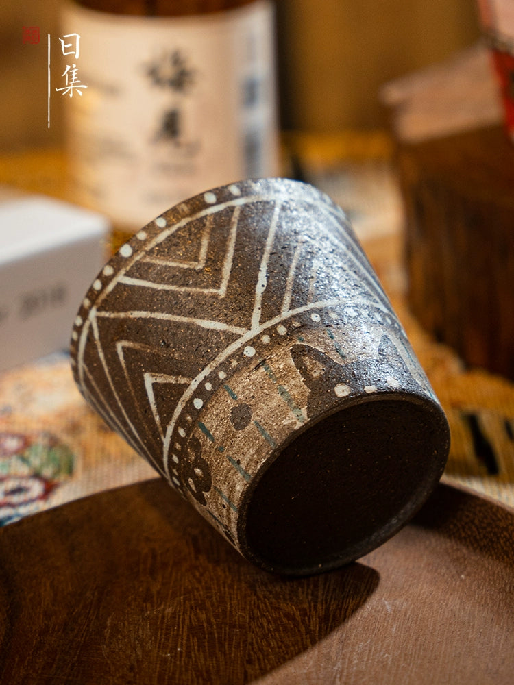 Brown traditional Japanese hand-painted ceramic tea cup with white geometric patterns and floral details.