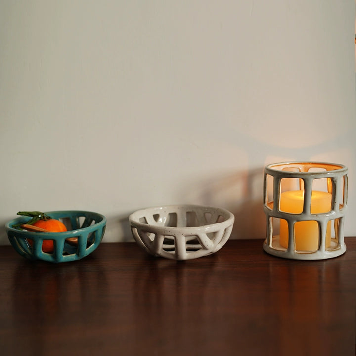 Two ceramic fruit bowls, one teal, one off-white, with a hollowed-out lattice design.  Handmade, displaying a tangerine.