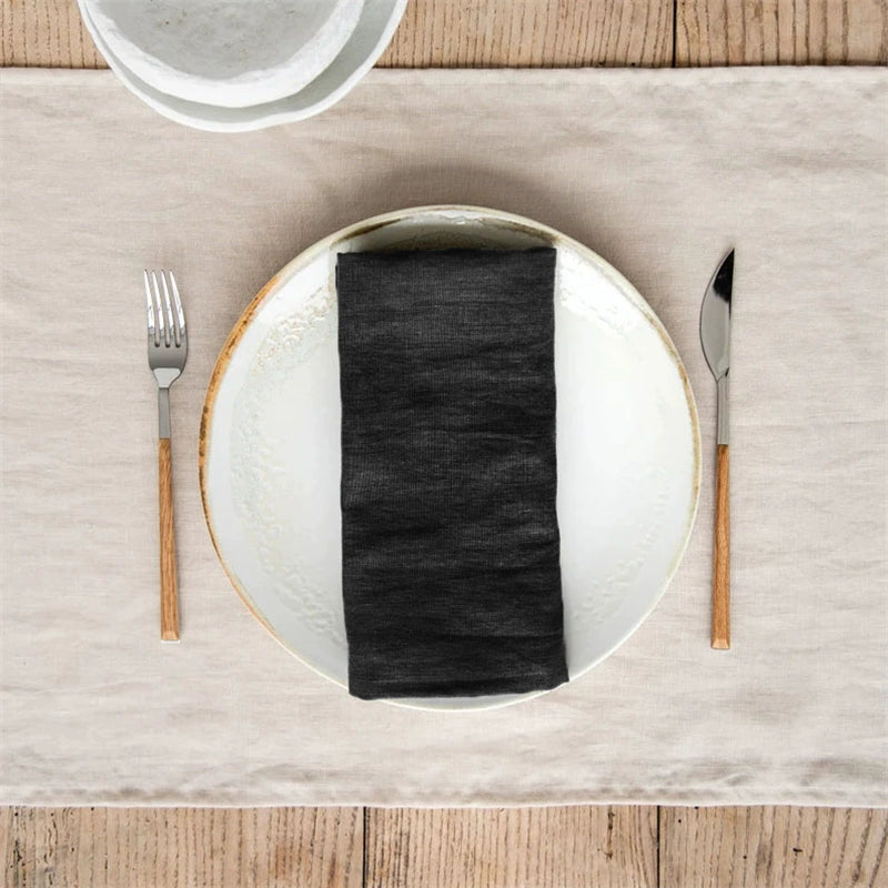 Black elegant linen table napkins, set of 4, neatly folded on a plate with silverware on a neutral runner.