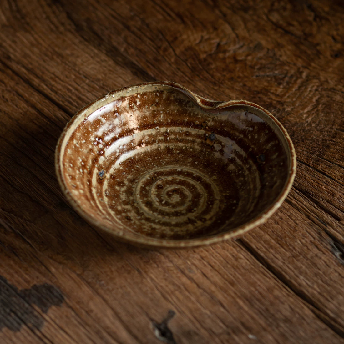 Top-down view of a small, heart-shaped ceramic bowl with a deep brown, swirling glaze pattern.